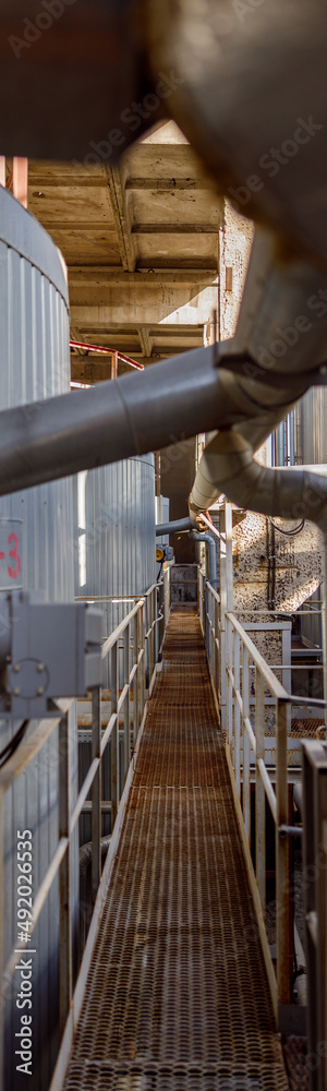 Section of manufacturing plant with pipes and metal bridge between industrial storage containers Section of manufacturing plant with pipes and metal bridge between industrial storage containers