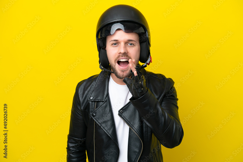 Fototapeta premium Young caucasian man with a motorcycle helmet isolated on yellow background shouting with mouth wide open