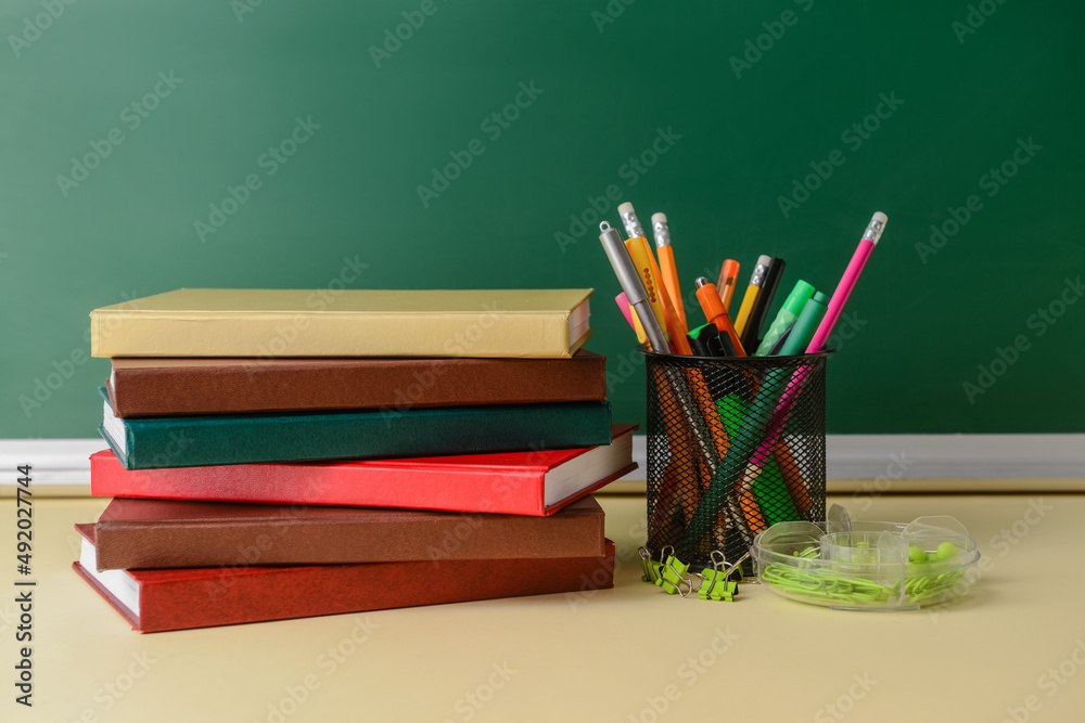 Stack of books and holder with stationery on table in classroom