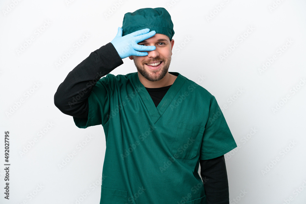 Surgeon in green uniform isolated on white background covering eyes by hands and smiling