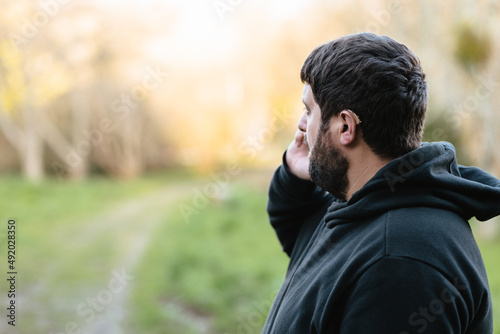 Hearing impaired man with hearing aid talks on the phone with his back turned