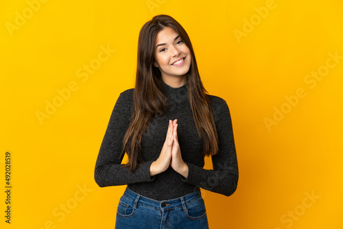 Teenager Brazilian girl isolated on yellow background keeps palm together. Person asks for something © luismolinero