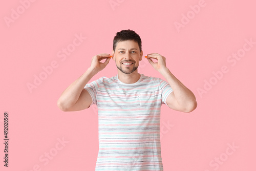 Handsome man putting ear plugs on pink background photo