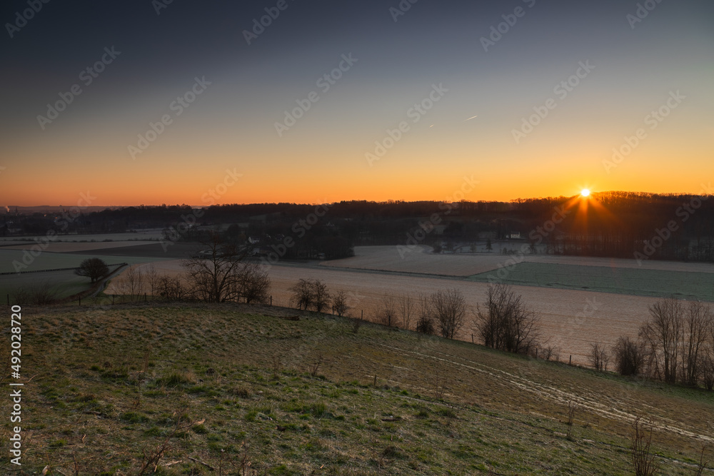 Fototapeta premium Sunrise over the Jeker valley with the vineyards near Maastricht with a view on the country border and the typical rolling hills landscape which this area is famous for.