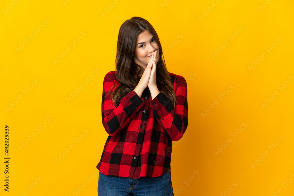 Teenager Brazilian girl isolated on yellow background keeps palm together. Person asks for something Teenager Brazilian girl isolated on yellow background keeps palm together. Person asks for something