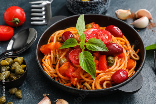 Frying pan with tasty Pasta Puttanesca and ingredients on dark background photo