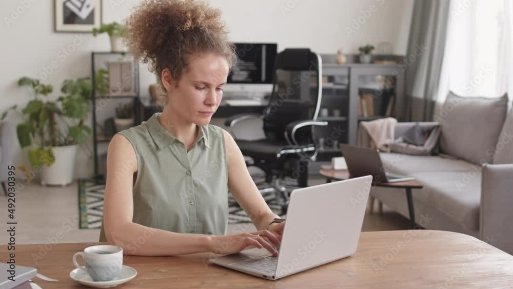 PAN medium shot of female programmer typing on computer and sipping her morning coffee while working at home office PAN medium shot of female programmer typing on computer and sipping her morning coffee while working at home office
