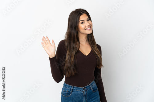 Teenager Brazilian girl isolated on white background saluting with hand with happy expression