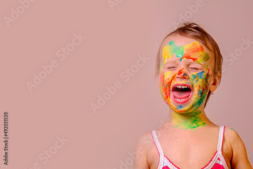 Humorous image of childrens makeup. Beauty, fashion, happy childhood concept. Portrait of beautiful young child girl with painted face and hands. Copy space for text or design. © zwiebackesser