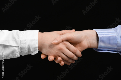 Business woman shaking man's hand on black background, closeup