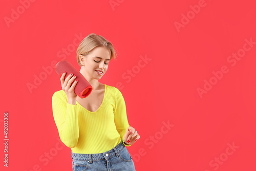 Young woman holding modern wireless portable speaker and dancing on red background