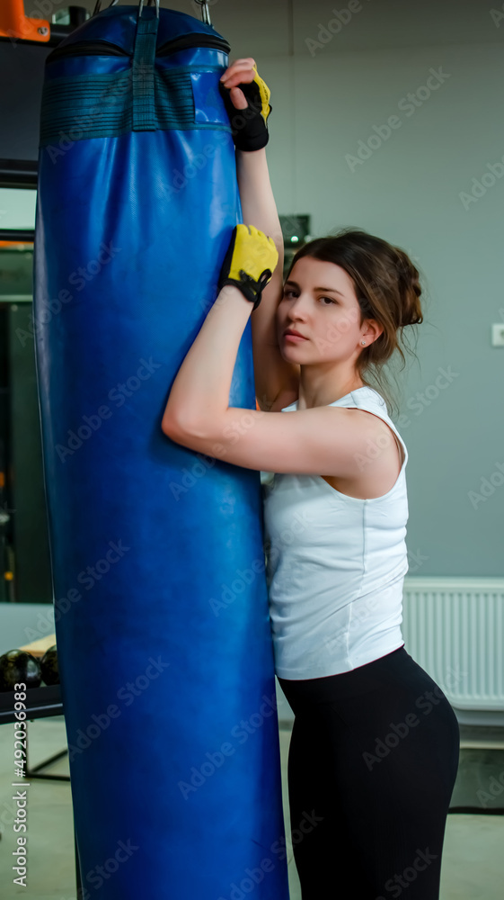sexy fighter girl in gym with boxing bag. Long hair woman fitness model resting after boxing