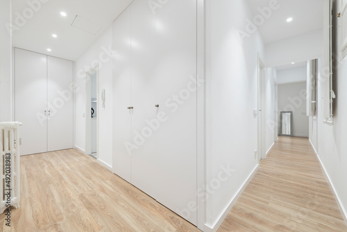 Hallway of a residential home with hardwood floors  white woodwork on doors and windows  and white painted walls  wood-framed mirror  and cast-iron radiator
