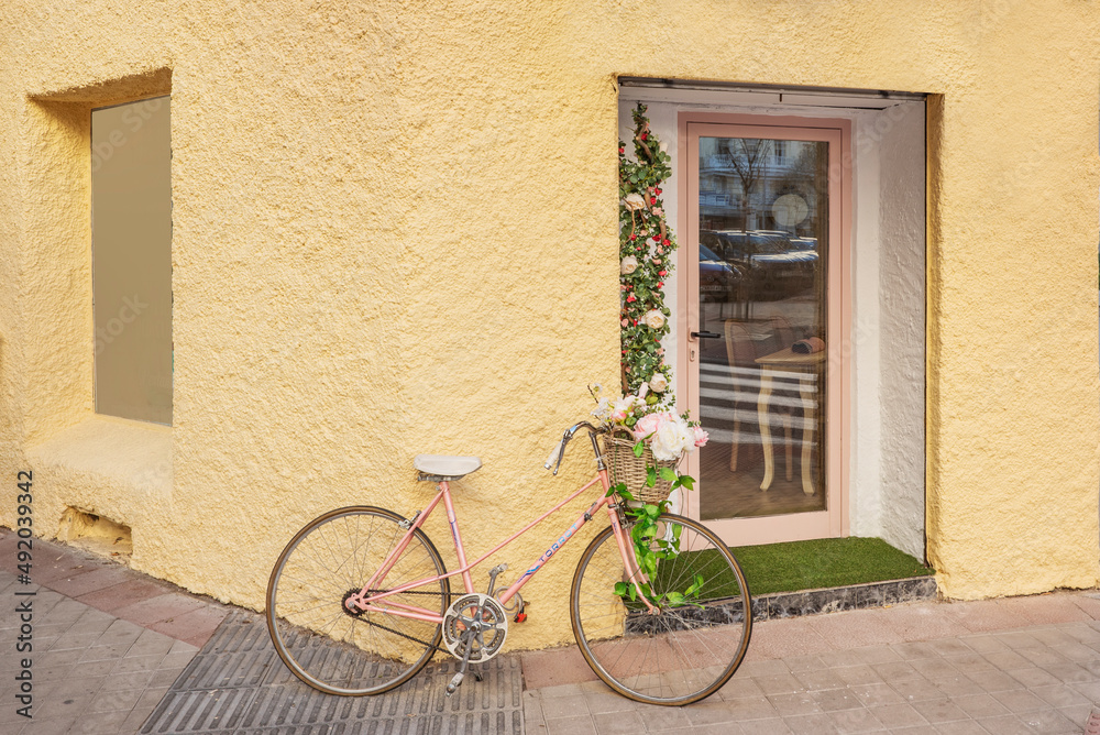 Pink bike parked on the wall of a yellow store with flowers