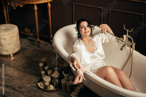 Wife at the photo session in studio. Married bride celebrate engagement. Procreation romantic amazing woman indoor, copy space. Preparing for wedding day, lying in bath and hold shoes heels
