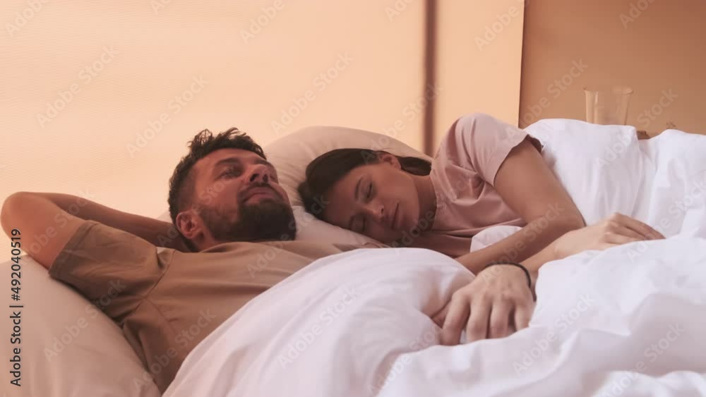 Young dark-haired Biracial woman and bearded husband sleeping in bed in hotel room in morning Young dark-haired Biracial woman and bearded husband sleeping in bed in hotel room in morning