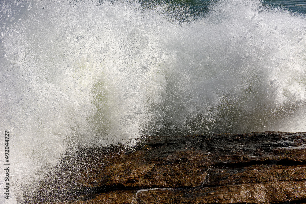 Strong wave breaking over rocks with water splashing in the air on a rough sea day in Rio de Janeiro, Brazil