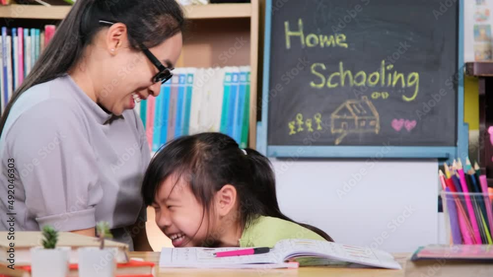 Asian little girl studies at home during quarantine with her mother. Mother helping little daughter with homework at home. Home schooling. Asian little girl studies at home during quarantine with her mother. Mother helping little daughter with homework at home. Home schooling.