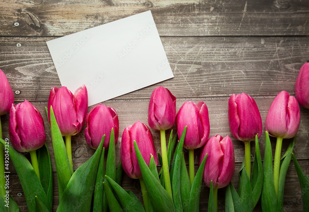 Fototapeta premium Pink Tulips and gift card on a wooden background. Space for the text. Top view