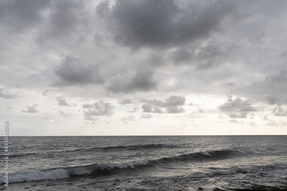 horizontal landscape view of a backdrop of ocean water under an expressive and cloudy sky