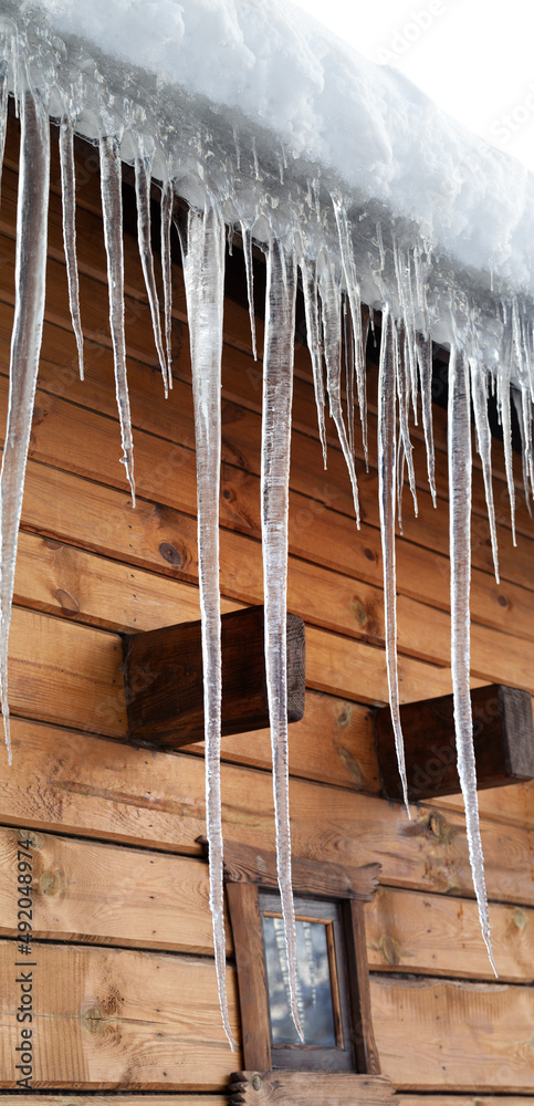 Wooden house with big icicles on snow-covered roof Wooden house with big icicles on snow-covered roof