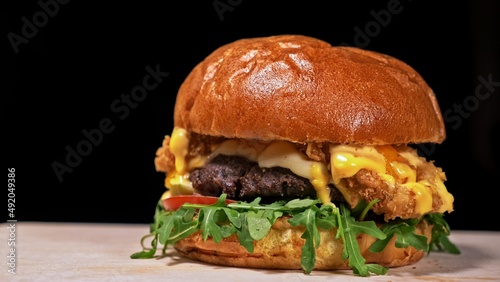 Craft burger is cooking on black background in black food gloves. Consist: sauce, arugula, tomato, red onion rings fries, cucumber, cheese, air bun and marble meat beef. Not made ideal. Looks real