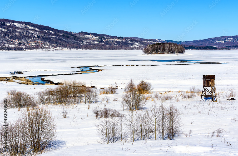 Φωτογραφία Winter landscape with a watch post and tributary River entering the frozen lake with with lake island and hills in the background background