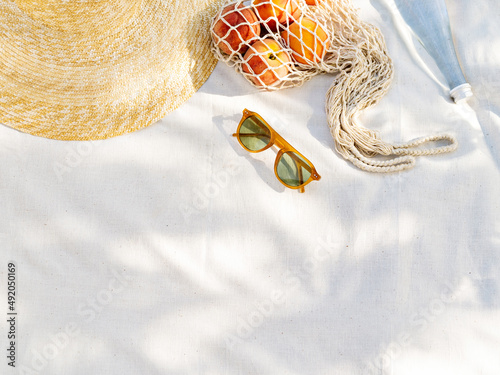 Vintage inspired background with straw hat, female sunglasses and shopper bag with peaches on white towel. Minimalist summer vacation creative still life ​for fashion blog, web, social media, stories.