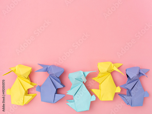 Easter paper decoration, seasonal pattern. Minimalist Easter border of handmade yellow and lilac paper bunnies. Greeting card, banner design. Origami paper craft. Spring holiday composition on pink.