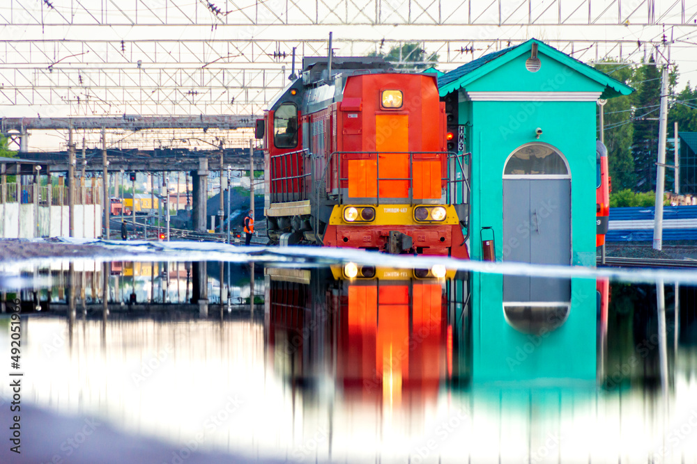 Obraz premium red diesel locomotive is reflected in huge puddle on platform formed from mistakes made in designing passenger platform