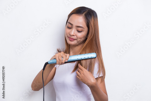 young asian beautiful happy woman straightening hair with hair straightener on white background 