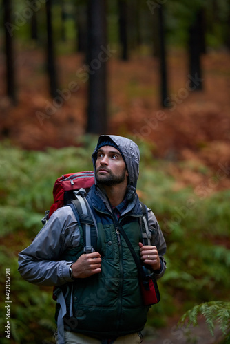 Lush, natural wilderness. Portrait of a young man wearing a backpack while hiking in the forest.