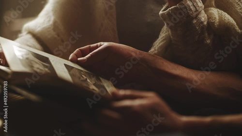 Rack focus of unrecognizable elderly couple inspecting aged pictures and turning page of vintage photo album while spending weekend day at home together