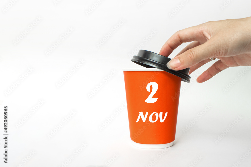 November 2nd. Day 2 of month, Calendar date. A woman's hand open black plastic cap of red disposable cardboard coffee paper cup with Calendar Date. Autumn month, day of the year concept. November 2nd. Day 2 of month, Calendar date. A woman's hand open black plastic cap of red disposable cardboard coffee paper cup with Calendar Date. Autumn month, day of the year concept.