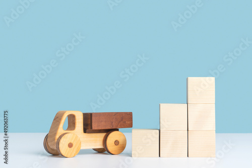 Photography A wooden toy car stands next to a pyramid ladder made of wooden cubes on a blue background