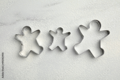 Gingerbread man cookie cutters and flour on white marble table, flat lay