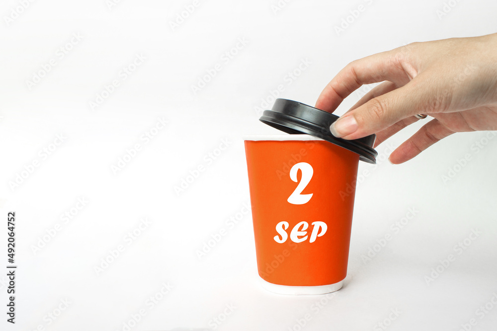 September 2nd. Day 2 of month, Calendar date. A woman's hand open black plastic cap of red disposable cardboard coffee paper cup with Calendar Date. Autumn month, day of the year concept. September 2nd. Day 2 of month, Calendar date. A woman's hand open black plastic cap of red disposable cardboard coffee paper cup with Calendar Date. Autumn month, day of the year concept.