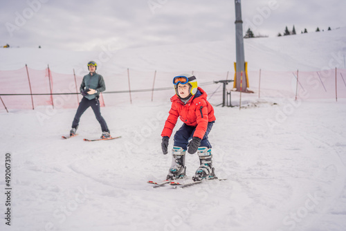 Boy learning to ski, training and listening to his ski instructor on the slope in winter