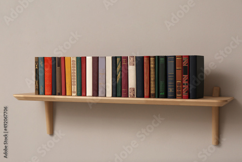 Wooden shelf with different books on light wall