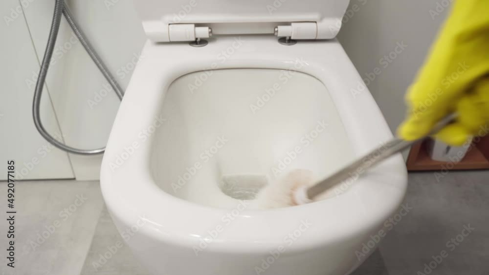 Woman's hand in yellow gloves cleans the toilet bowl with a brush and detergent, the concept of house cleaning and household chores. Woman's hand in yellow gloves cleans the toilet bowl with a brush and detergent, the concept of house cleaning and household chores.