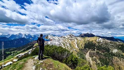Hiker man with backpack at summit of Hahnkogel (Klek) with scenic view on mountain peaks in Karawanks and Julian Alps, Carinthia, Austria. Border with Slovenia. Triglav National Park. Spreading arms