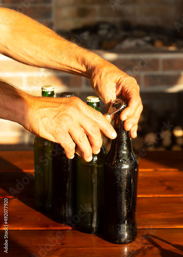 Male hands open a bottle of beer. Happy hour, golden sunset light illuminates the outdor patio.