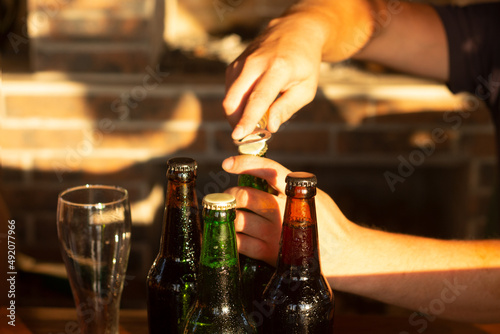Male hands open a bottle of beer. Happy hour  golden sunset light illuminates the outdor patio.