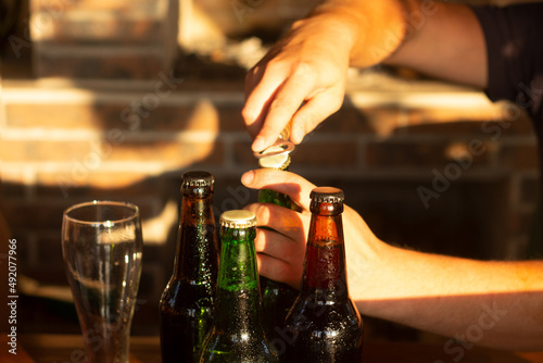 Male hands open a bottle of beer. Happy hour, golden sunset light illuminates the outdor patio.