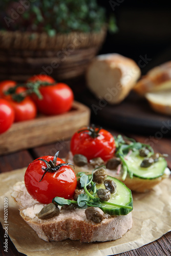 Tasty bruschettas with vegetables and capers served on wooden table, closeup