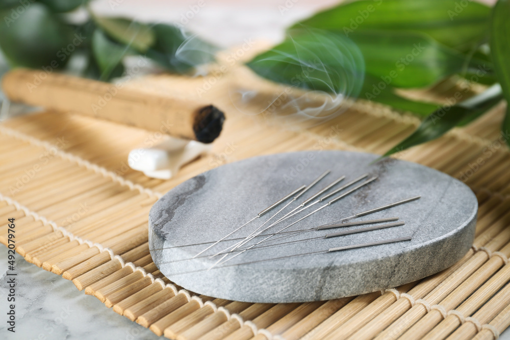 Grey stone coaster with acupuncture needles on bamboo mat - obrazy, fototapety, plakaty 