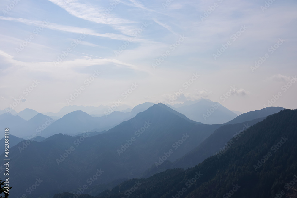 Fototapeta premium Scenic view on the alpine mountain chains of the Karawanks in Carinthia, Austria. Peaks are shrouded in morning fog. Mystical vibes. Clear and sunny day. Serenity. View from Ferlacher Spitze, Alps