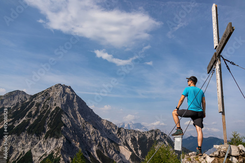 Man admiring the scenic view from summit cross of Ferlacher Spitze on Mittagskogel in the Karawanks, Carinthia, Austria. Borders between Austria, Slovenia, Italy. Julian Alps, Triglav National Park