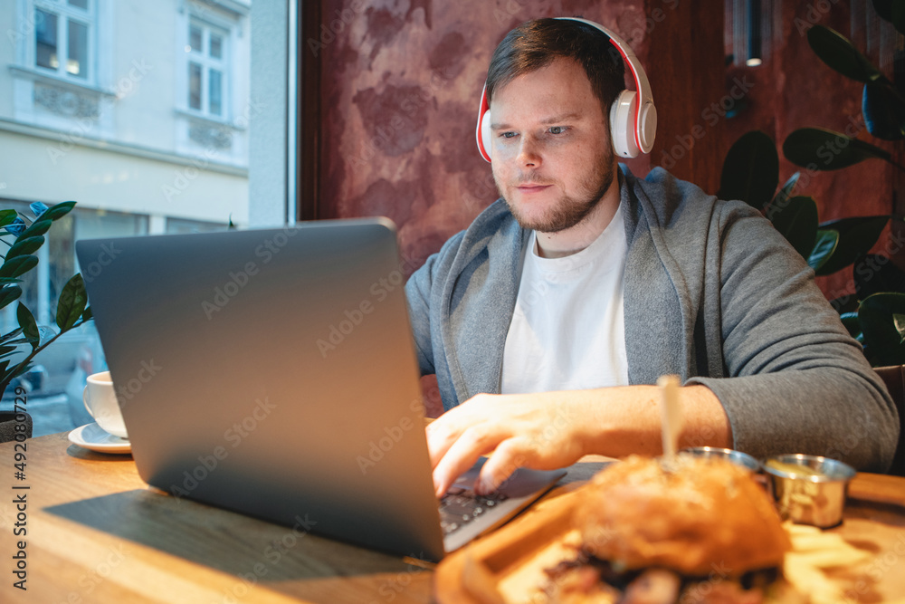 man freelancer working on laptop in cafe eating burger and drinking tea man freelancer working on laptop in cafe eating burger and drinking tea
