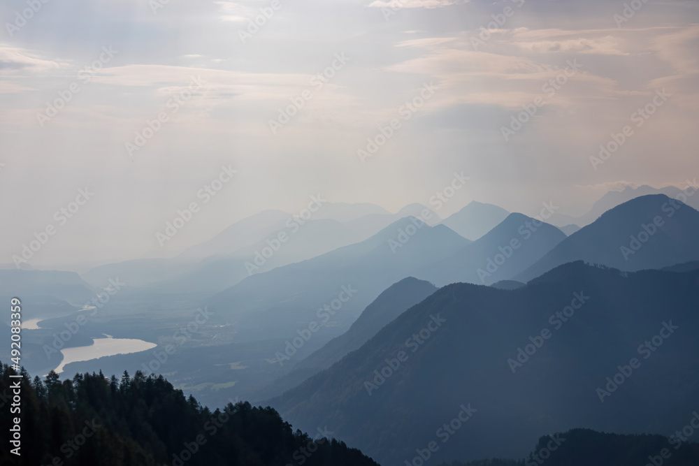 Scenic view on the alpine mountain chains of the Karawanks in Carinthia, Austria. Peaks are shrouded in morning fog. Mystical vibes. Clear and sunny day.  Serenity. View from Ferlacher Spitze, Alps